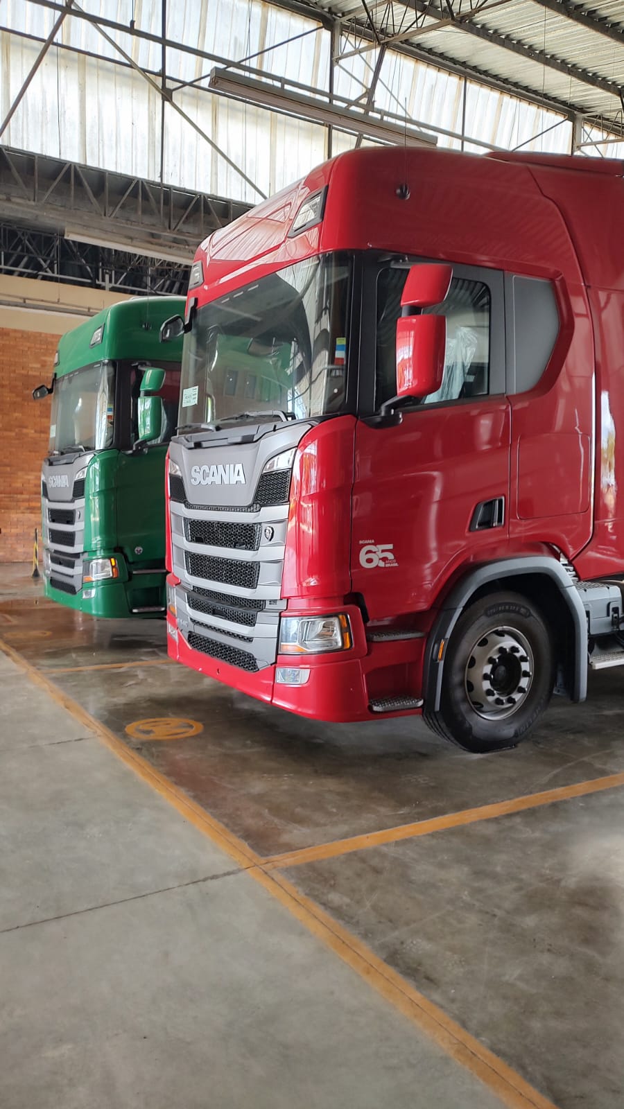 Caminhões Scania vermelho e verde em pátio coberto